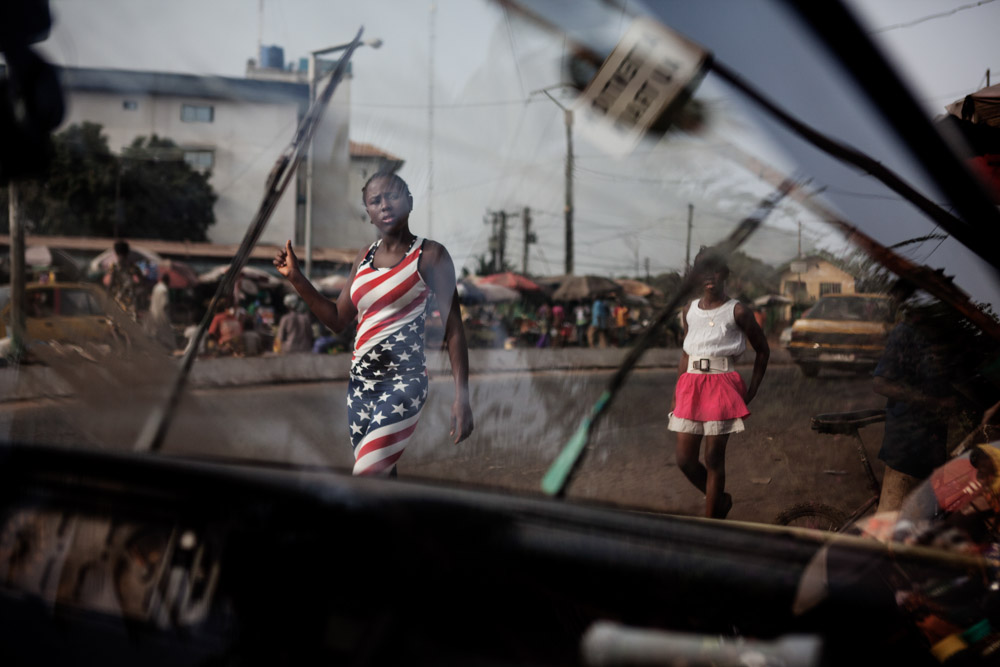 Girls walk passed a car being washed in Conakry, Guinea