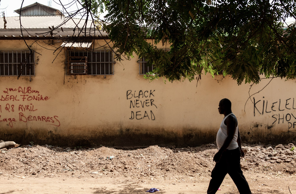 A man walks passed graffiti that reads {quote}Black Never Dead{quote} in Conakry, Guinea on January 27, 2015.