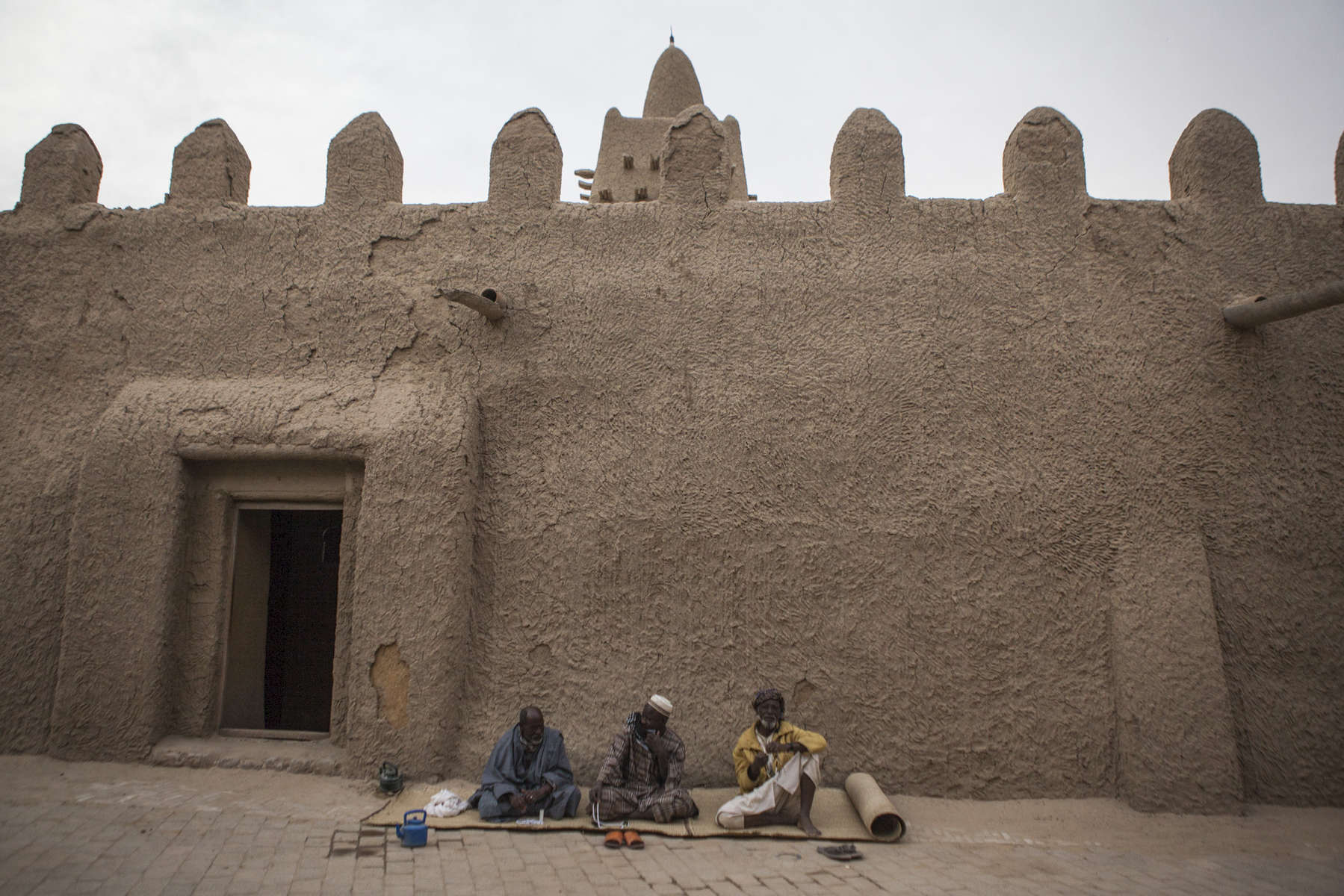 Men sit outside of the Sankore Mosque in Timbuktu, Mali on Monday, January 9, 2017. The Sakore Mosque was built in 1325 and is one of three learning centers in Timbuktu. It was partially destroyed during the occupation but has since been rebuilt. 