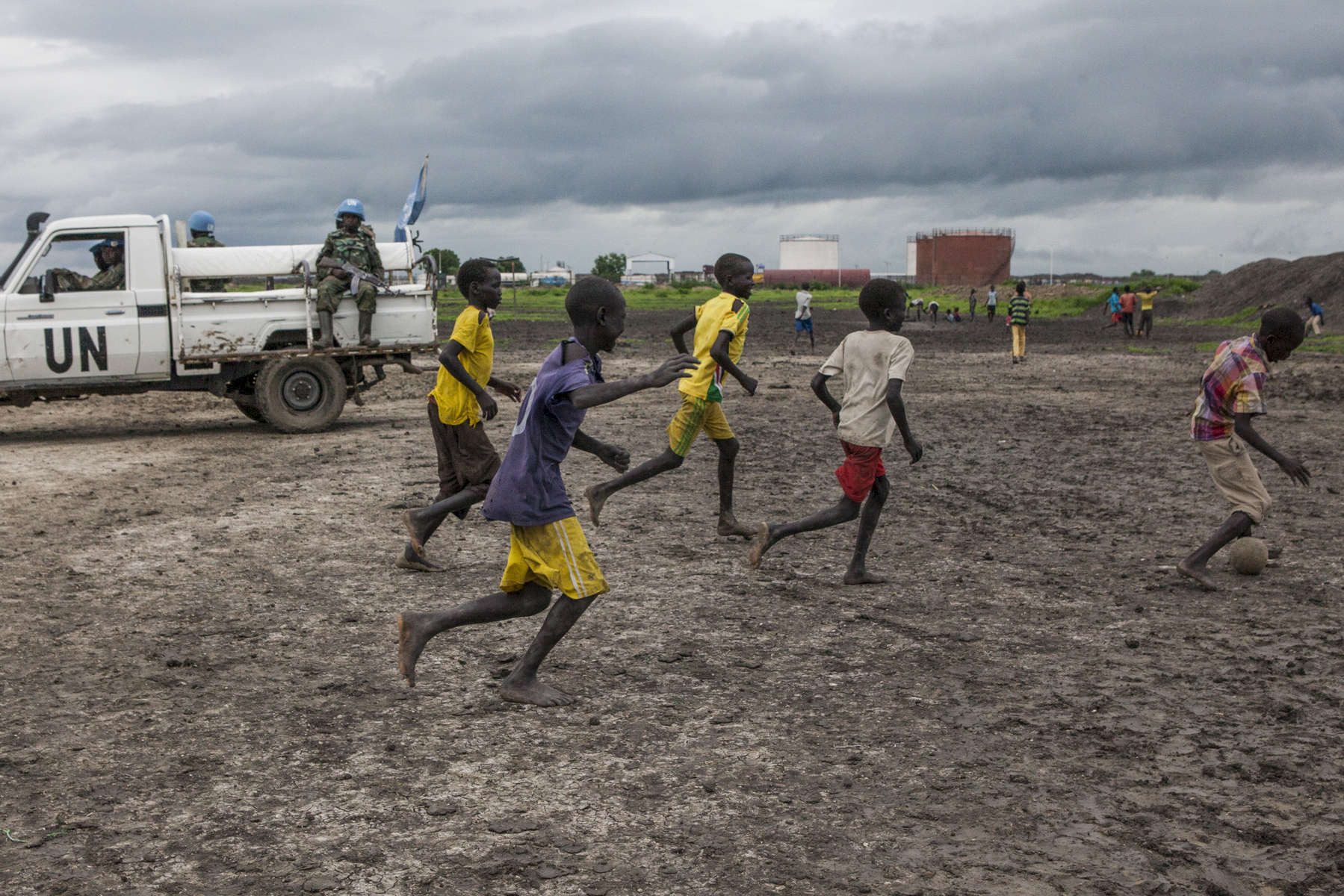 Boys play soccer in front of UN Peacekeepers at the Protection of Civilians (POC) site at the United Nations Mission in South Sudan (UNMISS) compound in Malakal, South Sudan on Wednesday, July 13, 2016. The Malakal POC site houses over 32,000 displaced people mainly from the Shilluk and Nuer tribes. In February of this year, members of the Dinka tribe, who resided in the camp at the time, carried out a coordinated attack within the site leading to the destruction of hundreds of shelters and many deaths. Since then, most members of the Dinka tribe have fled to Malakal town where they occupy the homes of those still displaced. 