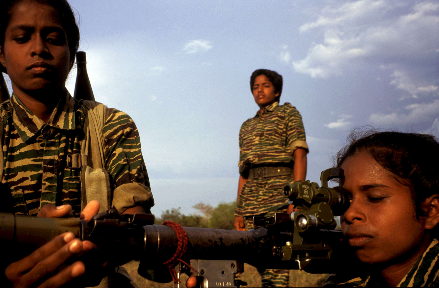 Female Tamil Tiger fighters during heavy weaponry training in the northern Vanni region of Sri Lanka. During a 6 month training period, the initial 3 months serve as an endurance testing ground beginning at 4:30 am until late evening. The training consists of long distance running, crawling under barbed wires, rope climbing, military parades coupled with theoretical and practical exercise with weapons, sentry posts staffed 24 hours, maintenance of the camp as well as political and military studies. The folowing 3 months is advanced military training with heavy weaponry and live ammunition - to familiarise both sound and impact.  Special training continues into areas of need, interest, and expertise in order to handle communication equipment, explosives, mining, weapon technology, electronics, field medecine, political work and intelligence/reconnaissance work. The women who show an aptitude for combat situations progress further to specialised commando training. 1998