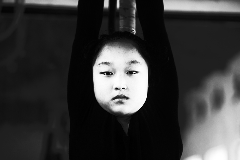 A young  acrobats ' apprentee hangs from a barre for about 30 minutes during daily excercises . Students who fail these kind of basic training  won't make it into a professional troupe.  