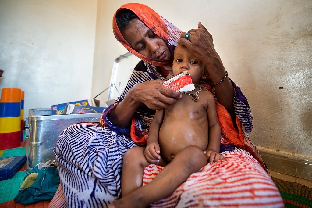 Aberahmanne\'s mother feeds him a Plumpy Nut (RUTF) during the appetite test at CRENAS centre in Mbera camp. Aberahmanne was brought in for screening by his mother who said that he had a fever and diarrhea.Anthropometric Measurement indicated that he is severely malnourished. Subsequent to examination and anthropometric measurements, Aberahmanne was diagnosed with Severe Acute Malnutrition (SAM) and will need to undergo appetite test before he is referred further to CRENI for clinical treatment of malnutrition.In Mbera refugee camp, the Nutrition survey carried out in November 2014 showed a significant decrease of both global acute malnutrition (from 11.8 to 9.9%) and severe acute malnutrition (1.4% to 0.8) rates. As of today, UNICEF has been supporting the government nutrition center in the treatment of 444 severe acute malnutrition (SAM) cases and contributed to the treatment of 790 other SAM cases. 