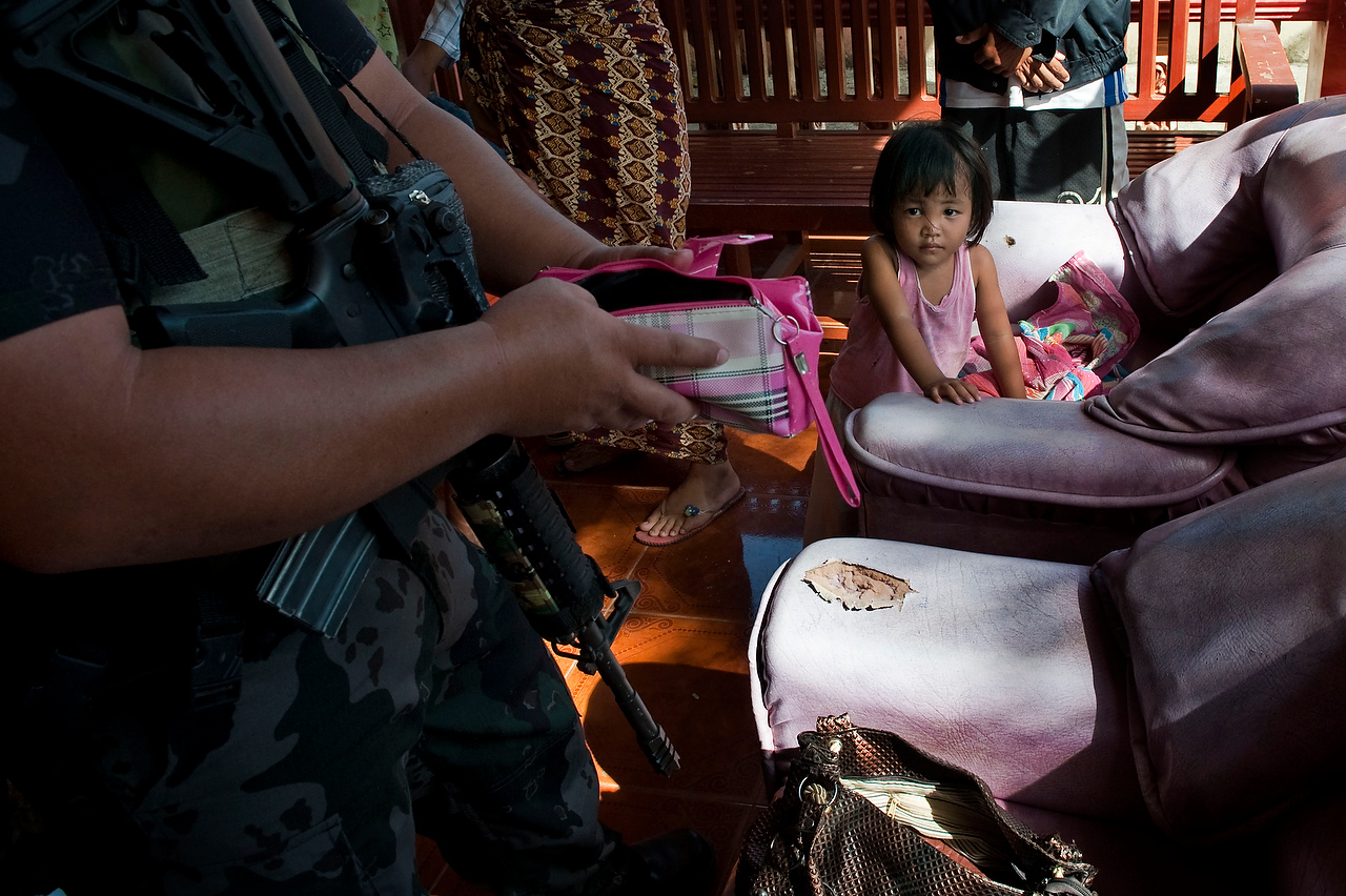 A child watches member of the special police force as he checks her mothers belongings during the raid which was allegedly orchestrated by the opponnent political candidate during the election campaign in Maguindanao.