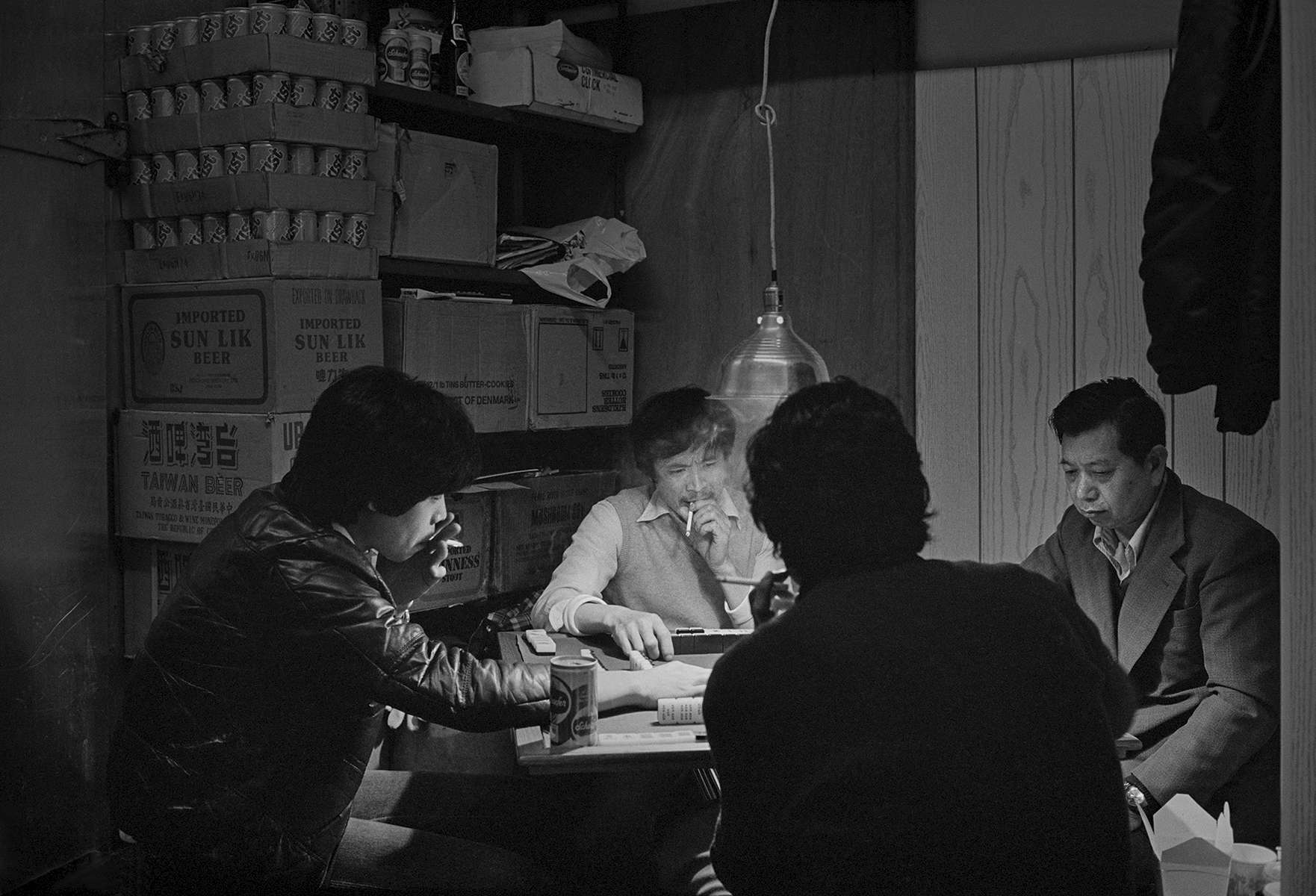 Men playing Mahjong in the back room of  Frankie Wong's butcher shop, Fook Hing Long, 27 Catherine St., New York Chinatown, 1981. Frankie's is seen in silhouette with his back to the camera.