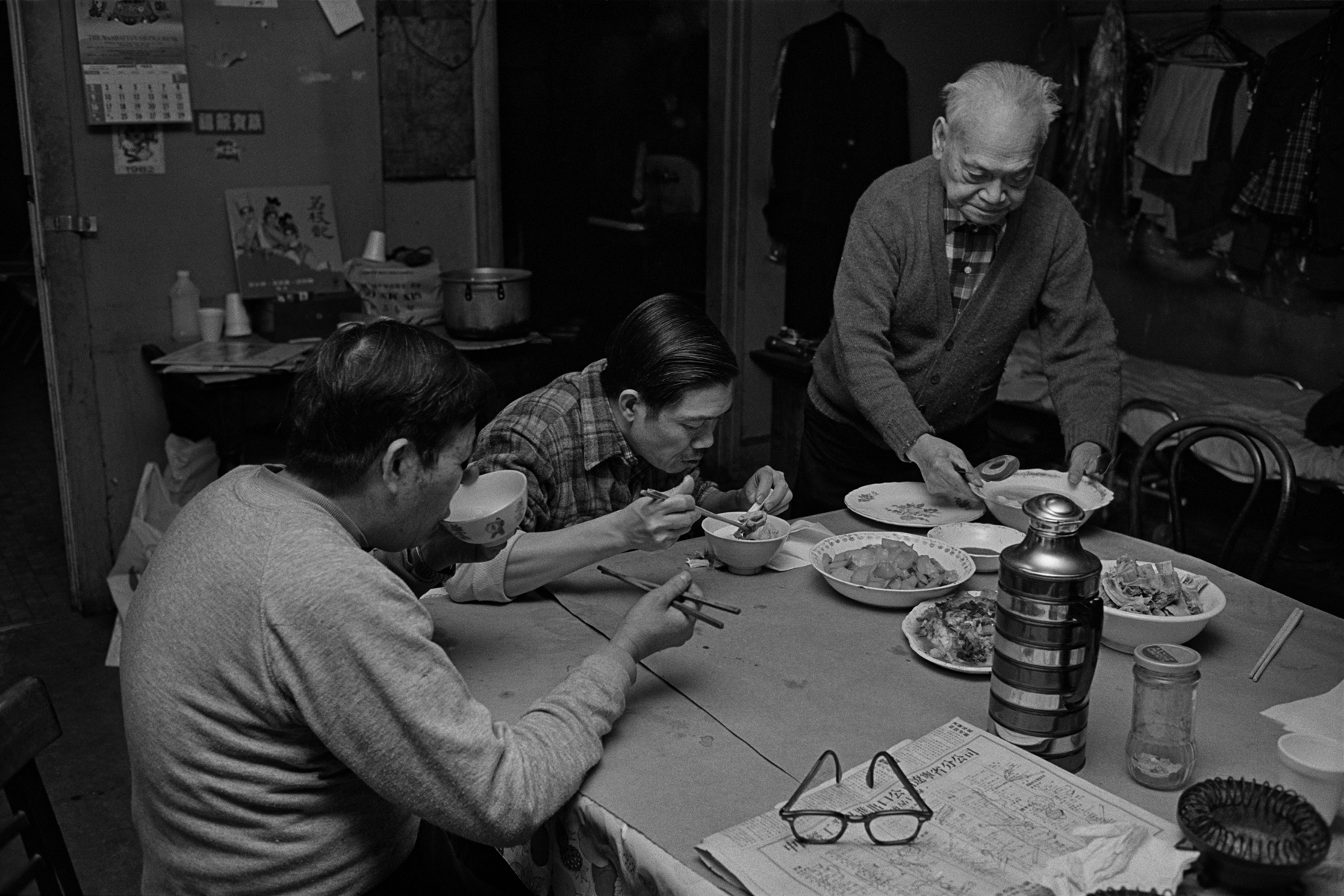 3 men at the common table eating dinner in Bachelor Apartment, they share on Bayard St., New York Chinatown, 1982