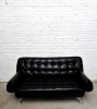 Black couch against white cinderblock wall in storage unit in Hoboken, New Jersey. By photographer Adena Stevens
