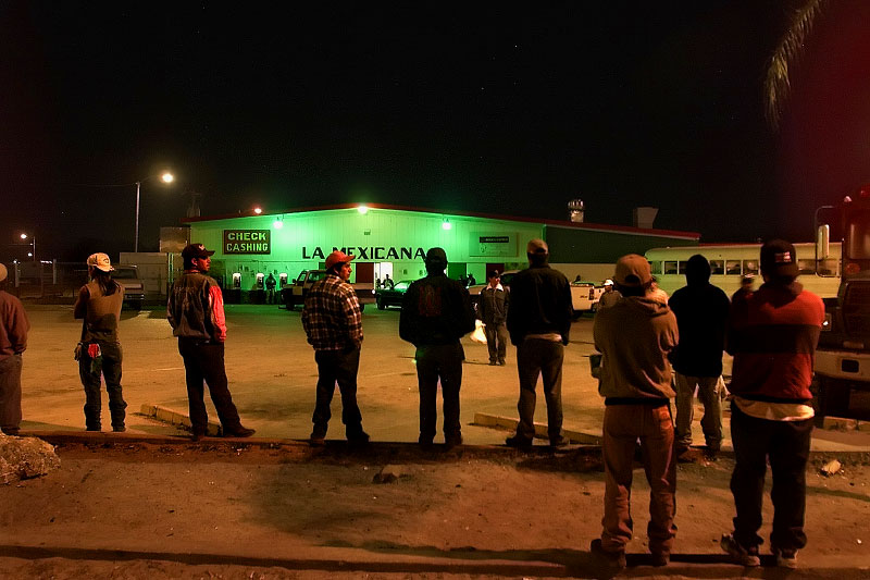 5:30 am, Immokalee farmworkers wait in the parking lot of La Mexicana grocery store where buses will come to pick-up day workers. Most wait for the regular bus and for others it's first come first serve for the seats that will take them to the fields. It's the end of the tomato picking season. 