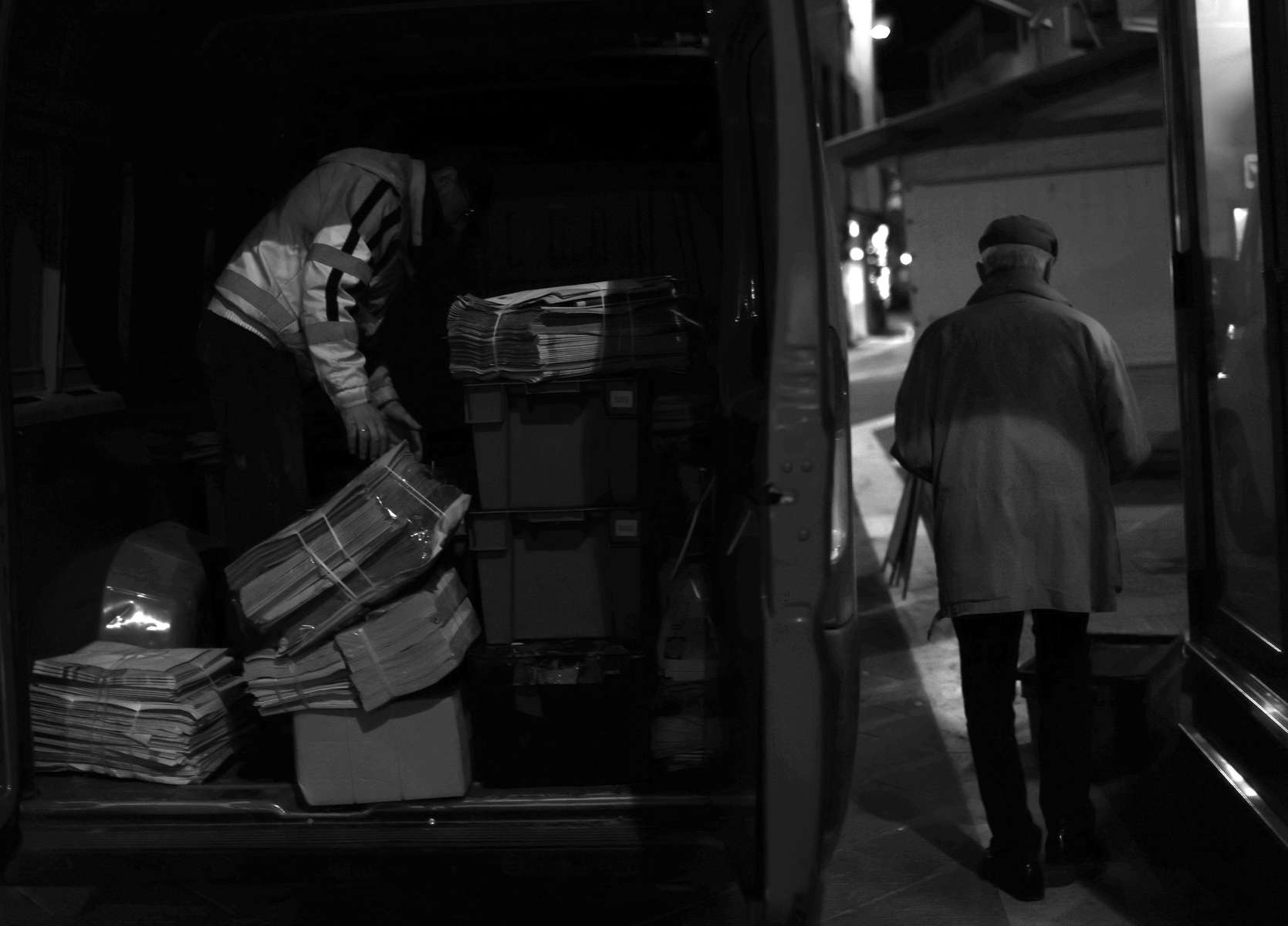 On November 25, 2024, while the city sleeps, newspaper delivery driver Paolo Camorri, left, unloads stacks of the day’s papers to Piero Scartoni, right.  Thousands of newsstands in Italy vanish each year.  One quarter of Italian towns no longer have a newsstand.  In the past twenty years, seventy percent of Italy's newsstands have closed.  