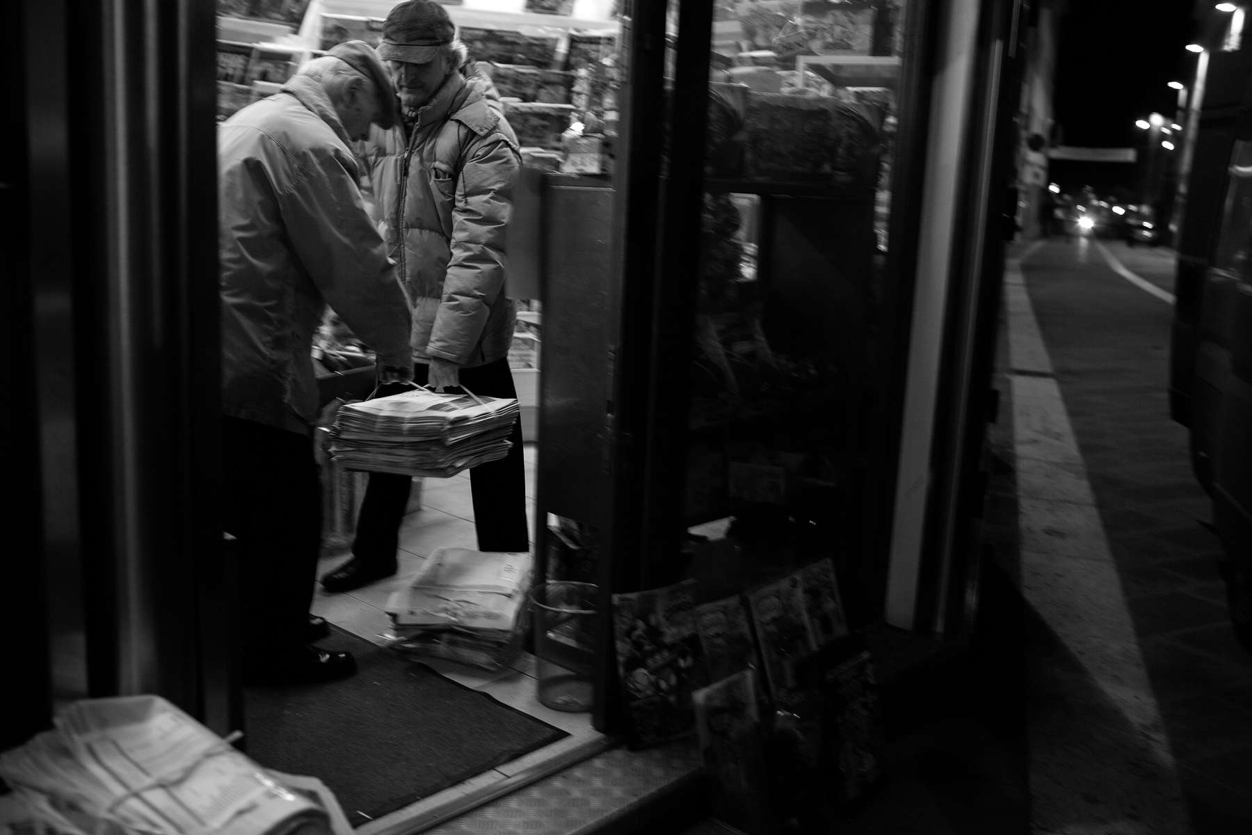 Early on the morning of November 15, 2023, Cesare Badii, right, helps Scartoni move newly delivered newspapers.  Later on this day, a car hits Scartoni's back bicycle wheel as he is returning to the newsstand for its afternoon hours.  A couple days later, back at work, he tells friend and newspaper delivery driver Paolo Camorri about the accident and how surprised he is that he has not broken anything to which Camorri replies, “L’acciaio non si rompe,” (steel doesn't break). 