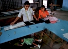 Two women work to sew their own clothes while the daughter of the woman at left takes a nap in La Carpio. Most families in the community can't afford to pay for someone to take care of their children while they work.