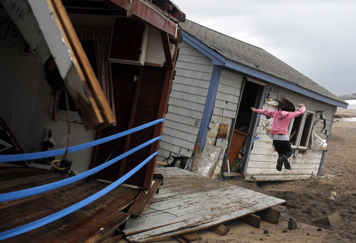 A girl jumps off the porch of a cottage along Roy Carpenter's Beach that was destroyed by Hurricane Sandy in Matunuck, Rhode Island October 30, 2012. 