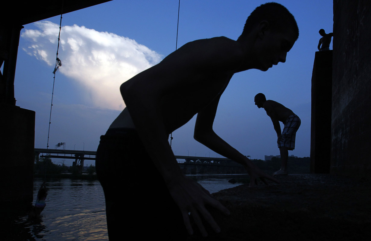 People are silhouetted as they play on a rope swing over the James River in Richmond, Virginia June 21, 2012.