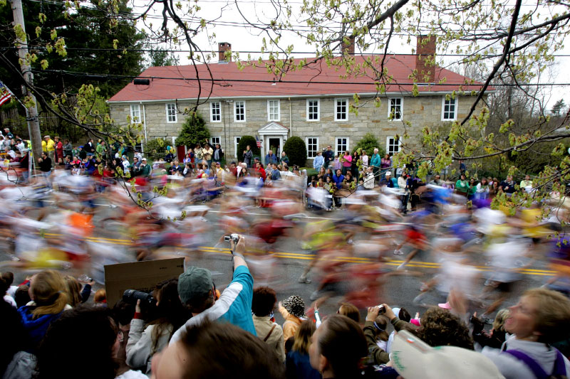 A man leans over to take a picture as runners stream past Hopkinton Center at the start of the Boston Marathon in Hopkinton, Massachusetts April 17, 2006. 