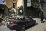 BAKU, AZERBAIJAN.  A man drives by in a convertible as a woman walks down the street beside a demolition site where a parking garage, park, and tunnel are planned after the government forced the eviction of several residents over several blocks to make way for the new project in the Besh Mertebe neighborhood on April 12, 2012.