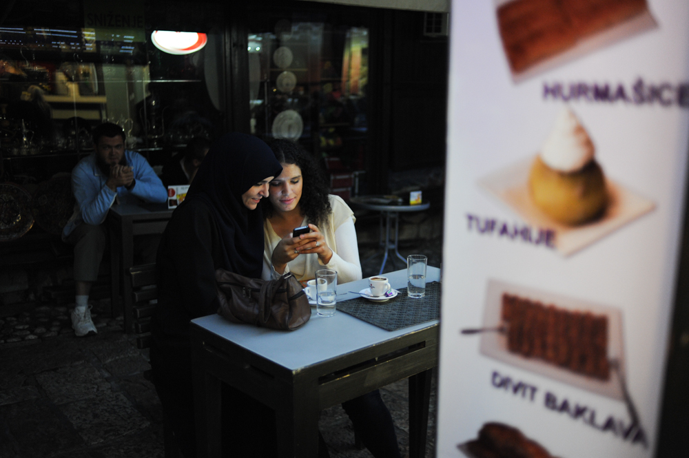 SARAJEVO, BOSNIA AND HERZEGOVINA.  Friends share a moment looking at cell phone pictures in front of a dessert shop in the old city on October 11, 2014.