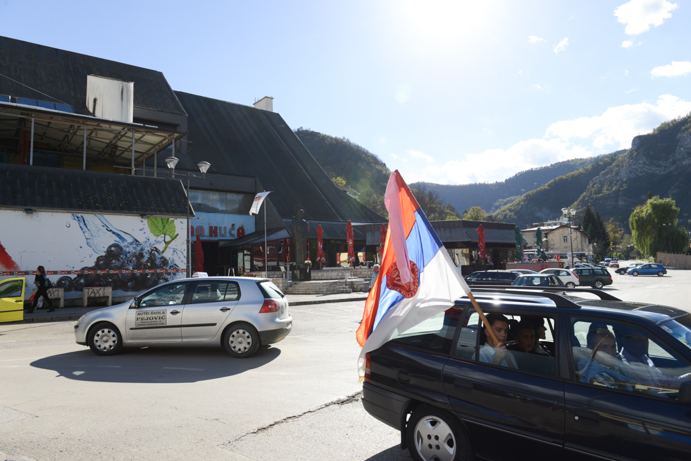 VISEGRAD, REPUBLIKA SRPSKA, BOSNIA AND HERZEGOVINA.  A man waves a Serbian flag as part of a wedding procession through the streets on October 18, 2014.  Visegrad was ethnically cleansed by the Bosnian Serb Army during the 1992-1995 conflict; a plaque on the statue beside the café in the background states, {quote}Monument to defenders of the Republika Srpska from the grateful people of Visegrad{quote}.