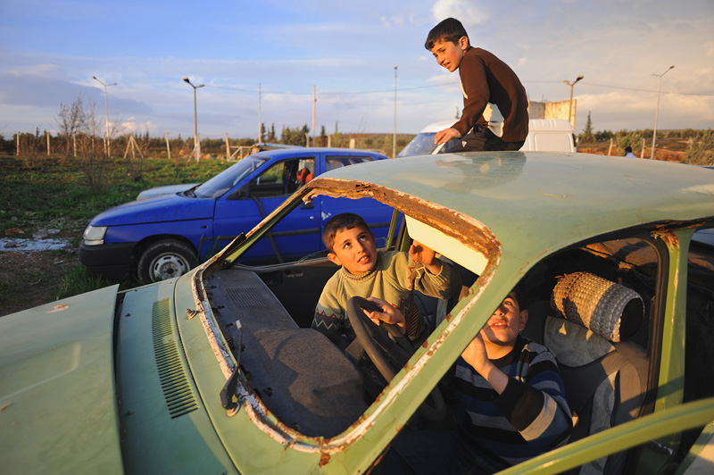 REYHANLI, TURKEY.  Syrian children play in a junkyard of old, abandoned and destroyed vehicles at the entrance to the Reyhanli tent city in Reyhanli, Turkey on February 26, 2012.  As the year old rebellion against the rule of Bashar Al-Assad continues just across the border in Syria, Turkey has seen a continued influx of refugees from the Syrian conflict but has not granted them refugee status and instead considers them to be {quote}guests{quote} of Turkey; Turkey's border with Syria is just one hour from the Ceyhan Marine Terminal where the Baku-Tbilisi-Ceyhan oil pipeline ends its 1,100 mile journey at the Mediterranean port.