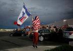 Kevin Abrahami jumps up and down as he waves a Democrat flag when a car passes with passengers showing solidarity with him at Clark County Election Department November 7, 2020, in North Las Vegas. Donald Trump supporters rally across the street from Abrahami.