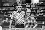 Barney and Pricie Rowe, Rowe’s Restaurant, Kyle, WVa, 1978. This combination restaurant/bar was like many in coal country, open early and late to accommodate miners working round-the-clock shifts. Men came in for beers after the graveyard shift ended, as others ate breakfast before starting work. The day I came by a fist fight broke out between two burly brothers in their late teens. A few punches were thrown, but it was quickly broken up. I was sitting with the woman pictured, whose husband was the owner. She got very teary and upset, despite no one getting hurt. When I asked why, she explained she hated to see brothers fight. She went on to relate how years earlier two brothers began fighting, and the place was getting torn up. Her husband told them to stop, to no avail. He raised his shotgun from behind the bar and repeated his demand. The two charged him, and he fired his gun. Seconds later, two brothers lay dead on the barroom floor. No charges were ever brought. That was justice in the back hills of West Virginia. Both Barney and Pricie, and their daughter Barbara, have passed away, and the restaurant no longer exists. Jon Chase photo