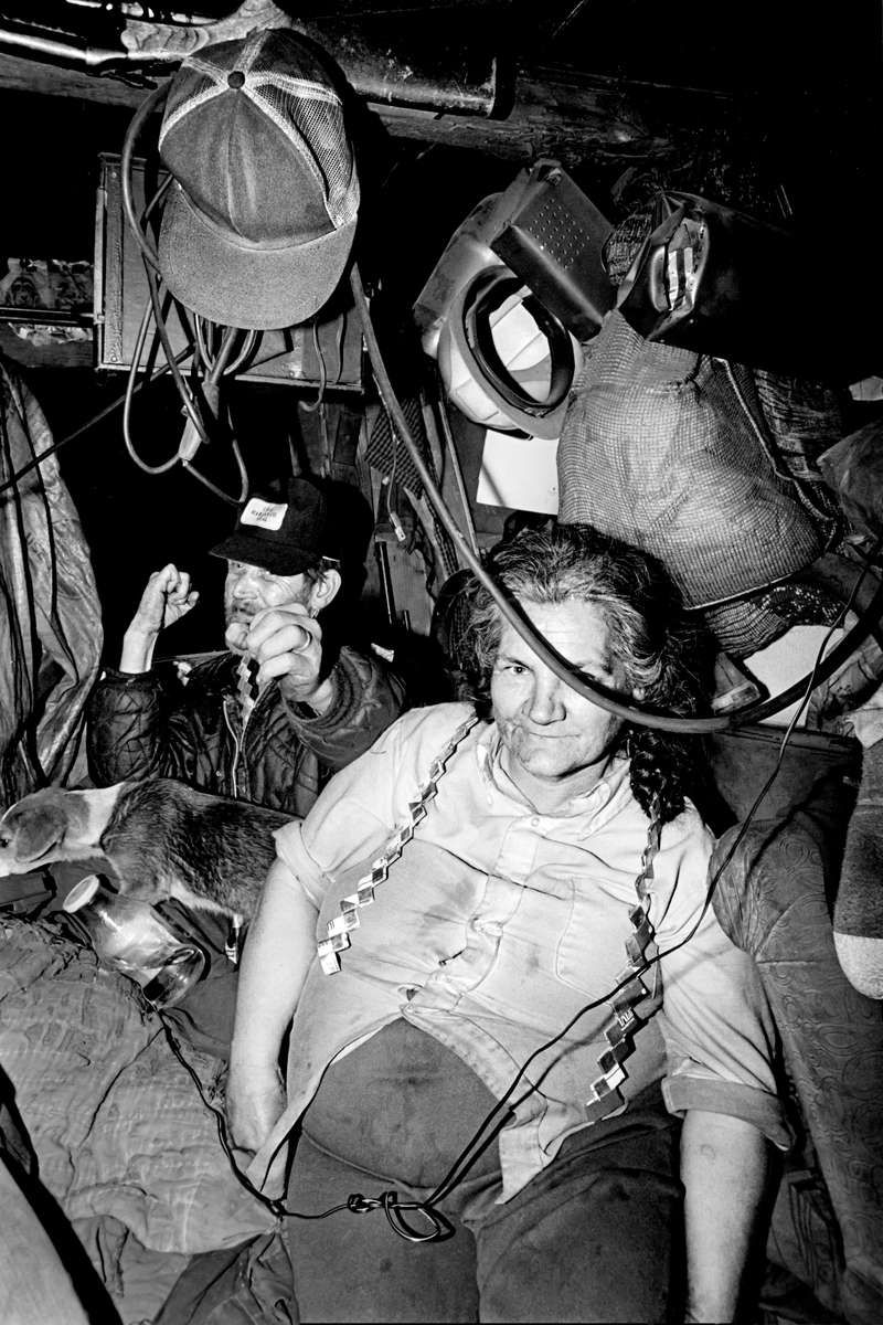 Coal miner Phelan Napier and wife in their one-room cabin, Harlan, KY, 1978. Phelan is putting up his dukes, perhaps an early sign of his increasing hostility during my visit, leading up to his holding us all hostage at gunpoint for two hours while threatening to shoot his wife. He lived off  disability checks, payment for injuries suffered in the mines. The emblem on his hat reads, “I dig Harlan Co (County) coal.” Jon Chase photo