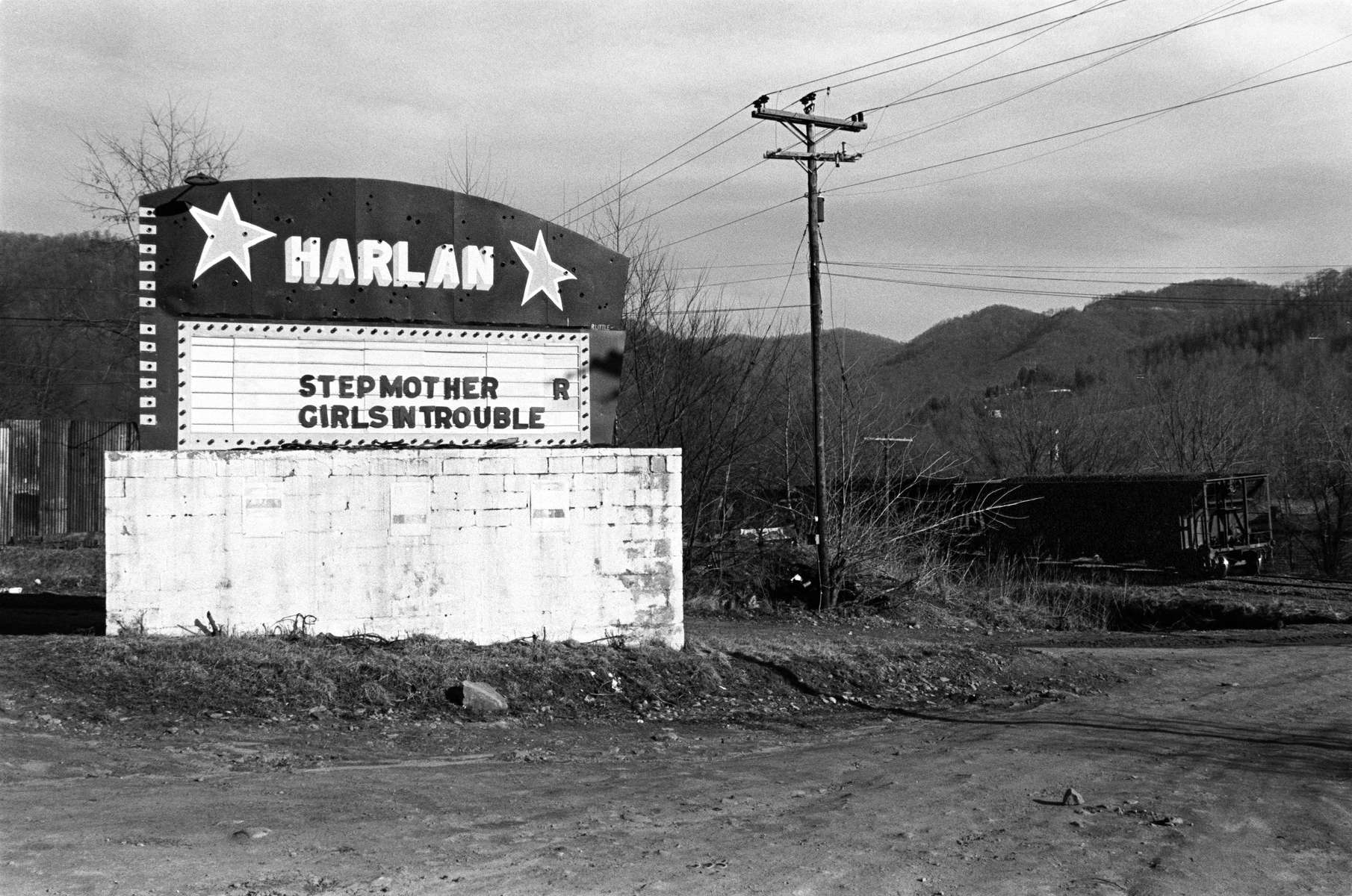 This marquee for a drive-in movie with a parked coal train on the right marks a desolate landscape after the theater closed and was demolished. Harlan has come to symbolize the hard-scrabble history of coal mining in Appalachia. Mining was dangerous work, with men occasionally trapped in collapsed mines resulting in multiple deaths. The Harlan Coal Wars lasted from 1931 to 1939, with numerous miners, deputies, and bosses killed. Strikes marked by violence continued for decades afterward. Underground mines began closing in the late 1970's, replaced by mountain-top removal and large-scale surface strip mining that scarred the landscape and polluted water sources. Jon Chase photo.