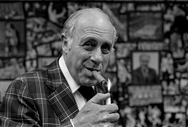 Surrounded by basketball photos spanning four decades, Boston Celtics president Red Auerbach lights up one of his trademark {quote}victory{quote} cigars.