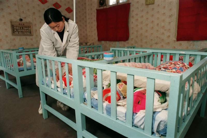 A nurse cares for babies, two to four in a crib, at the Children's Welfare Institute in Hefei, Anhui Province.