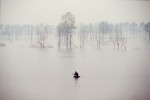 Solitary man fishing from innertube in flooded field, Hubei province, China.