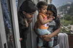 Esica Garcia Acevedo, 32, holding her nice, Kendy Camilo, 2, and her daughter, Francenny Acevedo, 14, left, on their balcony in Nuevo Occidente, a massive social housing complex, of mostly displaced or forced evicted families, in Medellin, Colombia. 18 family members live in a 70 square meter apartment given to them by the city in order to relocate the family from Moravia, a former garbage dump turned garden. The family's world takes place mostly inside their apartment. The children do not play outside because the parents say its too dangerous with speeding motorbikes and bad neighbors. The family says the city promised parks and programs for the children, but it never came. They often miss their old neighborhood.