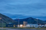 Exterior view of the Cache County Public Works Facility nestled up against the mountains in Hyrum, UT. The building is a metal and slate clad structure that is low in profile and modern looking and the picture was captured at dusk with the interior lights on.