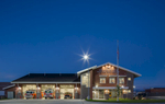 Exterior view of fire station at dusk with bay doors open and fire trucks in bays. Architectural Photography by: Paul Richer / RICHER IMAGES
