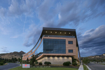 Exterior, architectural photograph of a modern biotech building under blue skies at dusk. The building is triangular in shape with a concave wall. The exterior is brick and glass and has an overhung roofline. on the bottom left is the Bio Fire signage. 