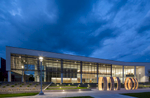 Exterior view of transparent college building at dusk with illuminated art in front and stormy blue skies.Architectural Photography by: Paul Richer / RICHER IMAGES