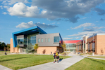 Exterior view of classroom wing with students walking to calss at sunrise at Mt. Jordan Middle School in Sandy Utah for MHTN Architects / Hogan & Associates. These wings feature metal cladding and overhangs of blue metal. Architectural Photography by Paul Richer / RICHER IMAGES