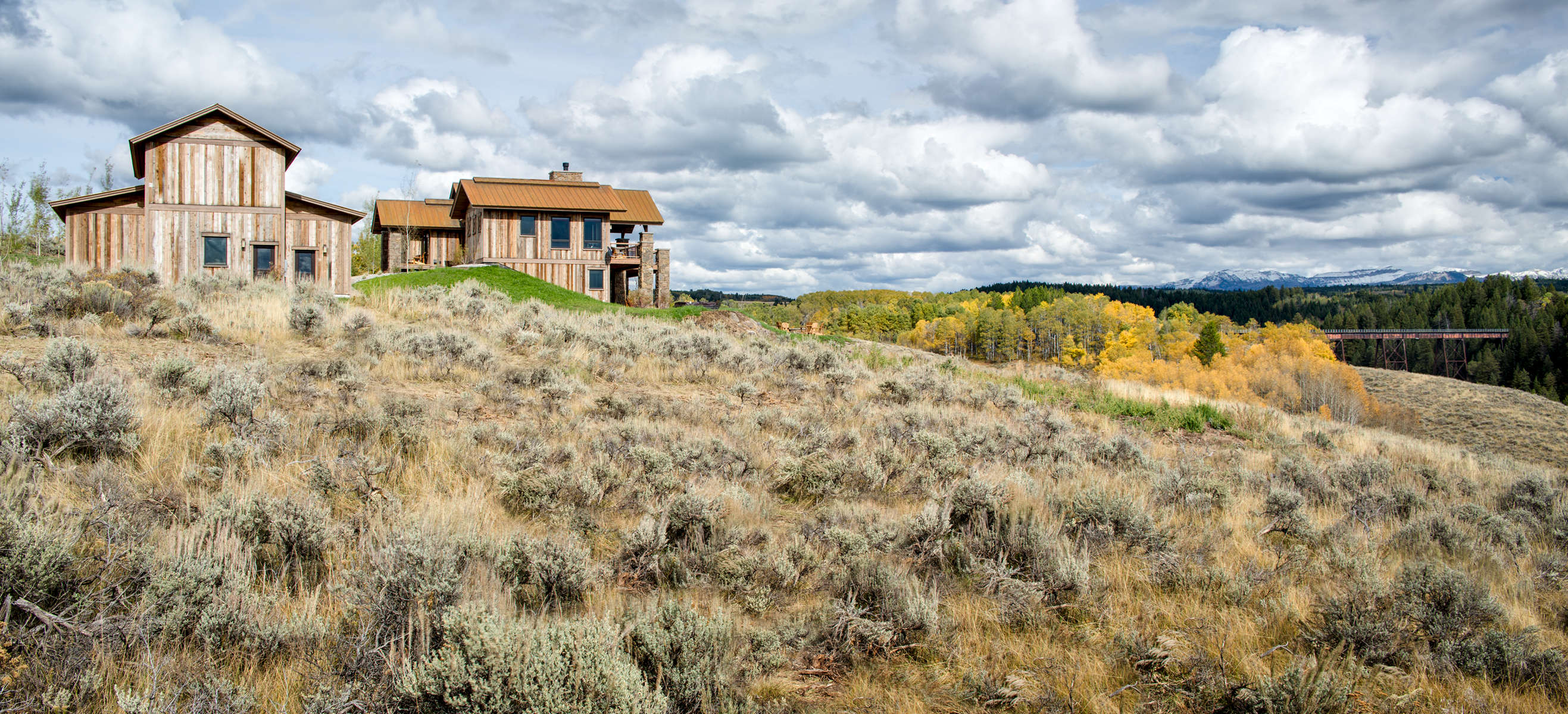Long distance view of a mountain rustic home surrounded by rolling hills and golden stands of Aspen trees in eastern Idaho.The viewer can also see an old train trestle which has been converted to a bike path.