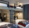 This is an interior photograph of a bunkroom for kids in a mountain modern rustic residence. There are four beds in all and the lower beds have built in cubbies with individual wall lights. There are pillows and black steel rails and a ladder.