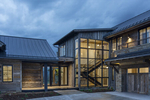 Exterior photograph of luxury residence at dusk near Park City, Utah. The photograph shows the main entrance with large glass windows that exposes the viewer to a beautiful stairwell  on the interior. The exterior of the home is of reclaimed lumber.