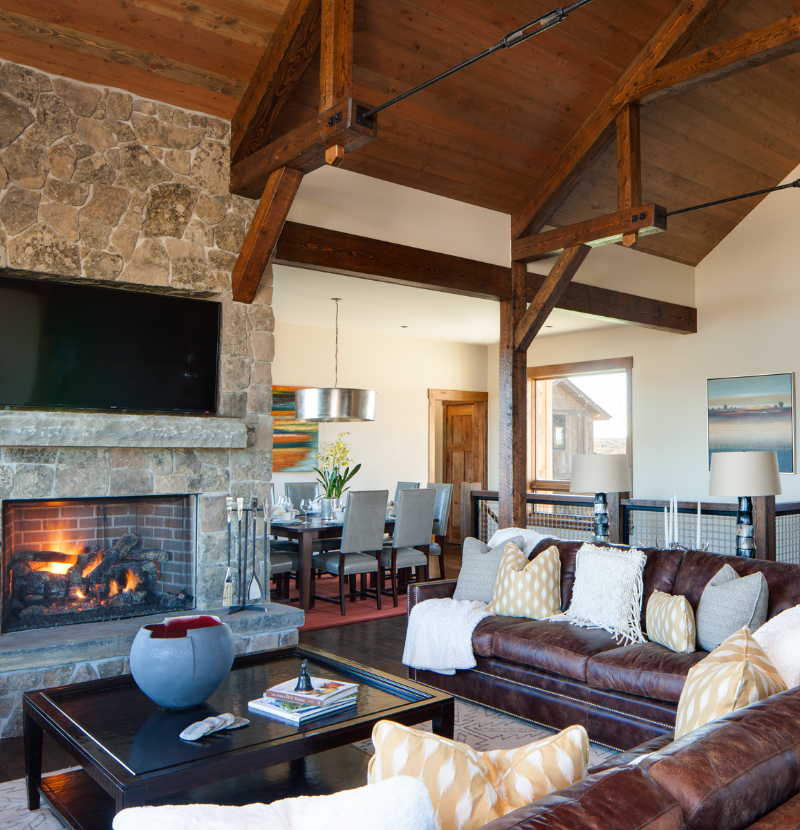 View of main living room in a mountain rustic home in eastern Idaho. The dining area can be seen in the back of the photo and in the forgrround we see a lit fireplace with a coffee table and a leather couch.Architectural Photography by: Paul Richer / RICHER IMAGES.
