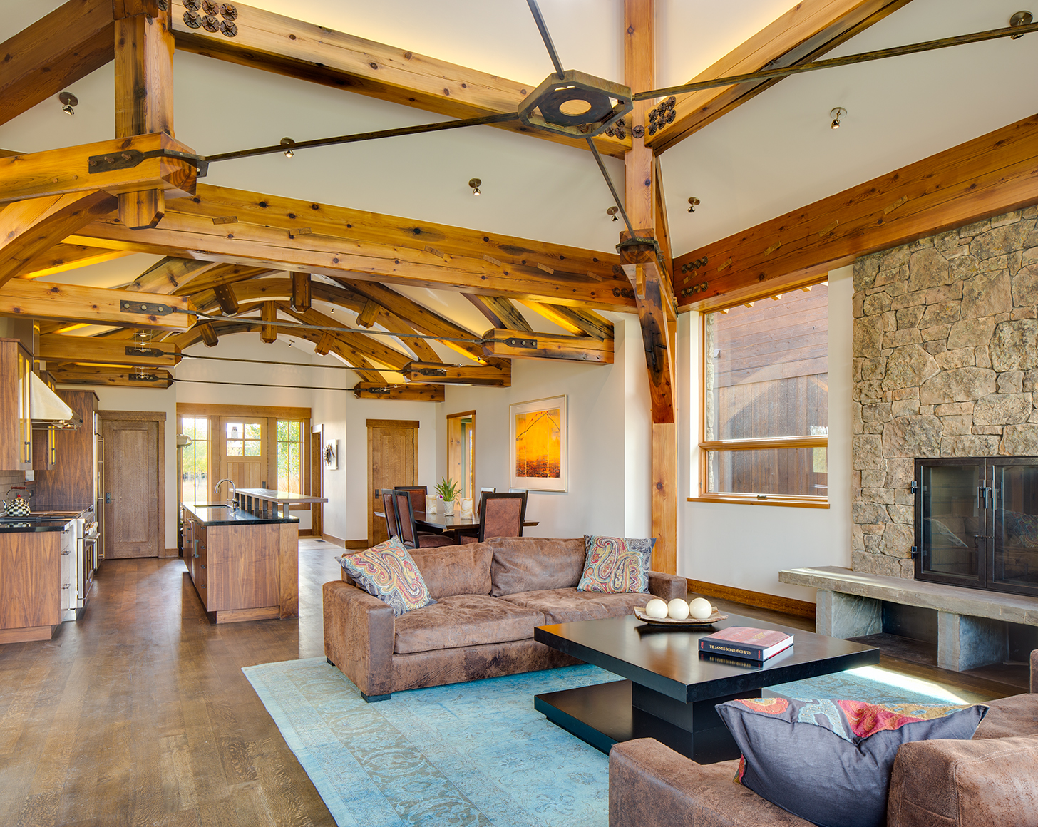 Interior view of main living area with kitchen, living room, fire place and dining room in private residence in Jackson, WY. The architectural high light is the exposed truss work of reclaimed timber.