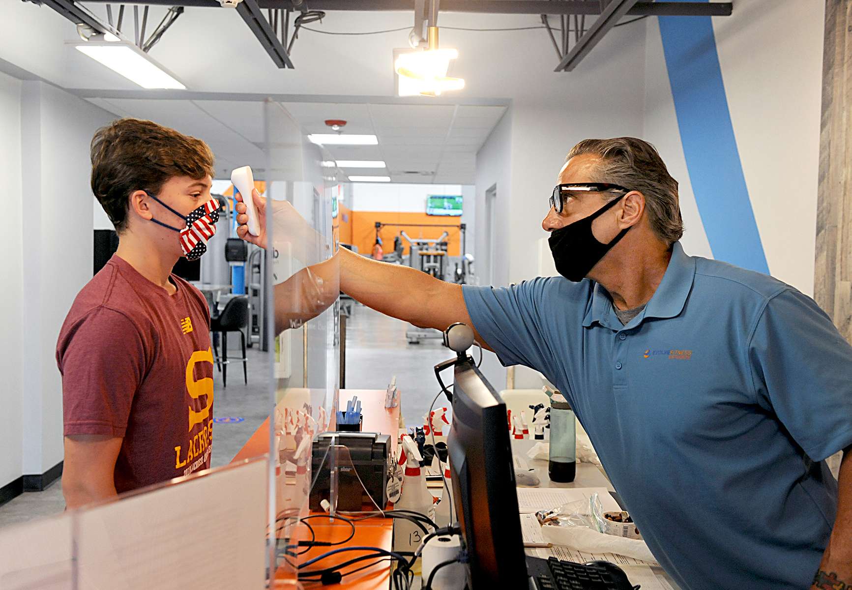 7/6/20-- FRAMINGHAM-- Phase 3 of Massachusett's reopening plan allowed fitness clubs to reopen with new guidelines. Evolve Fitness and Studios opened at 6 a.m. Monday. Pictured, front desk associate Frank Saldi, right, takes the temperature of Charlie David, 16, of Southborough. [Daily News and Wicked Local Staff Photo/Art Illman]