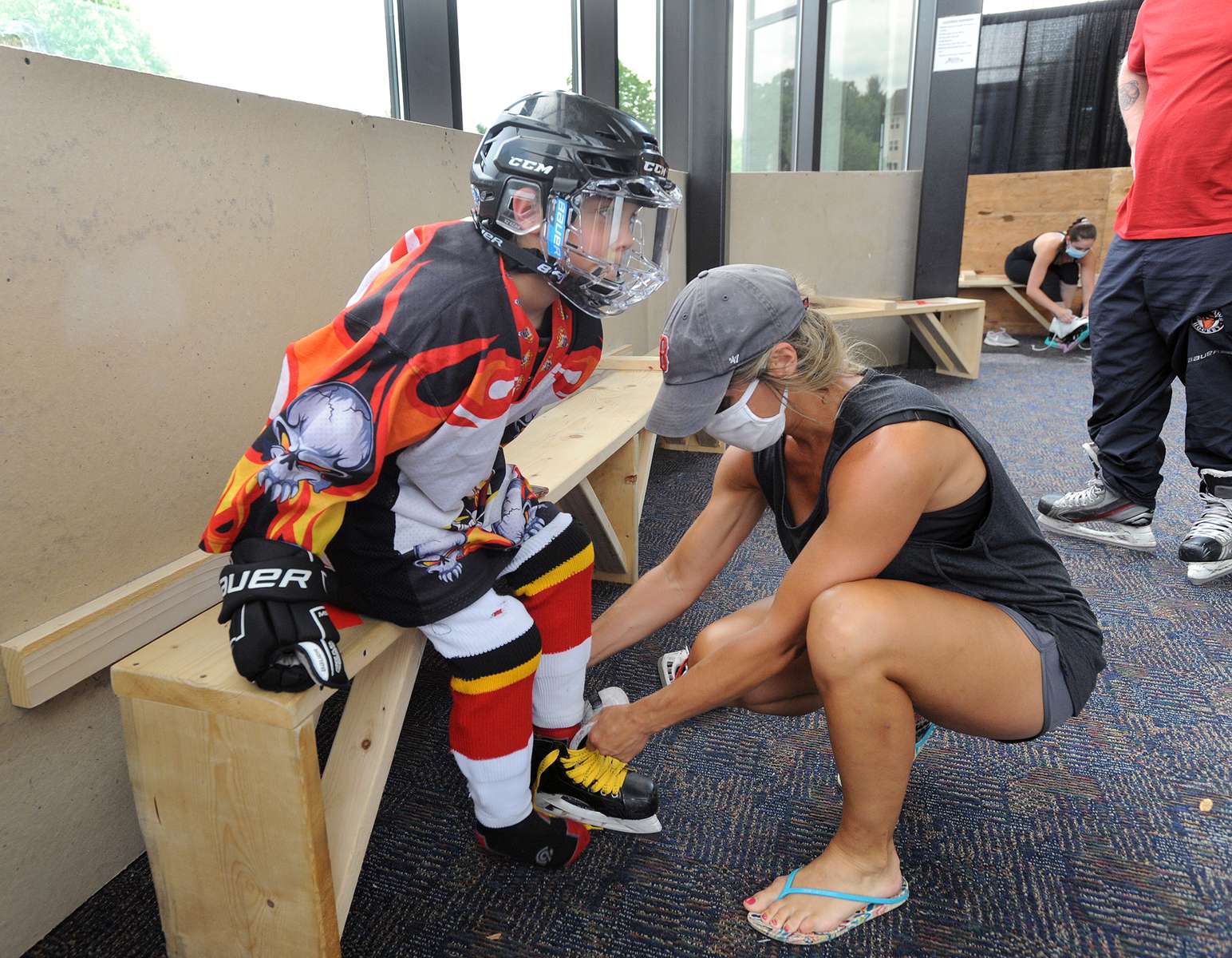 8/13/20-- MARLBOROUGH-- Sarah Argentieri of Shrewsbury laces up the skates of her 9-year-old son, Orazio, in a new socially distanced blocked off area in the lobby of the New England Sports Center before his private lesson on the ice Thursday. Locker rooms are closed so players arrive dressed in their uniforms.  [Daily News and Wicked Local Staff photo/Art Illman]