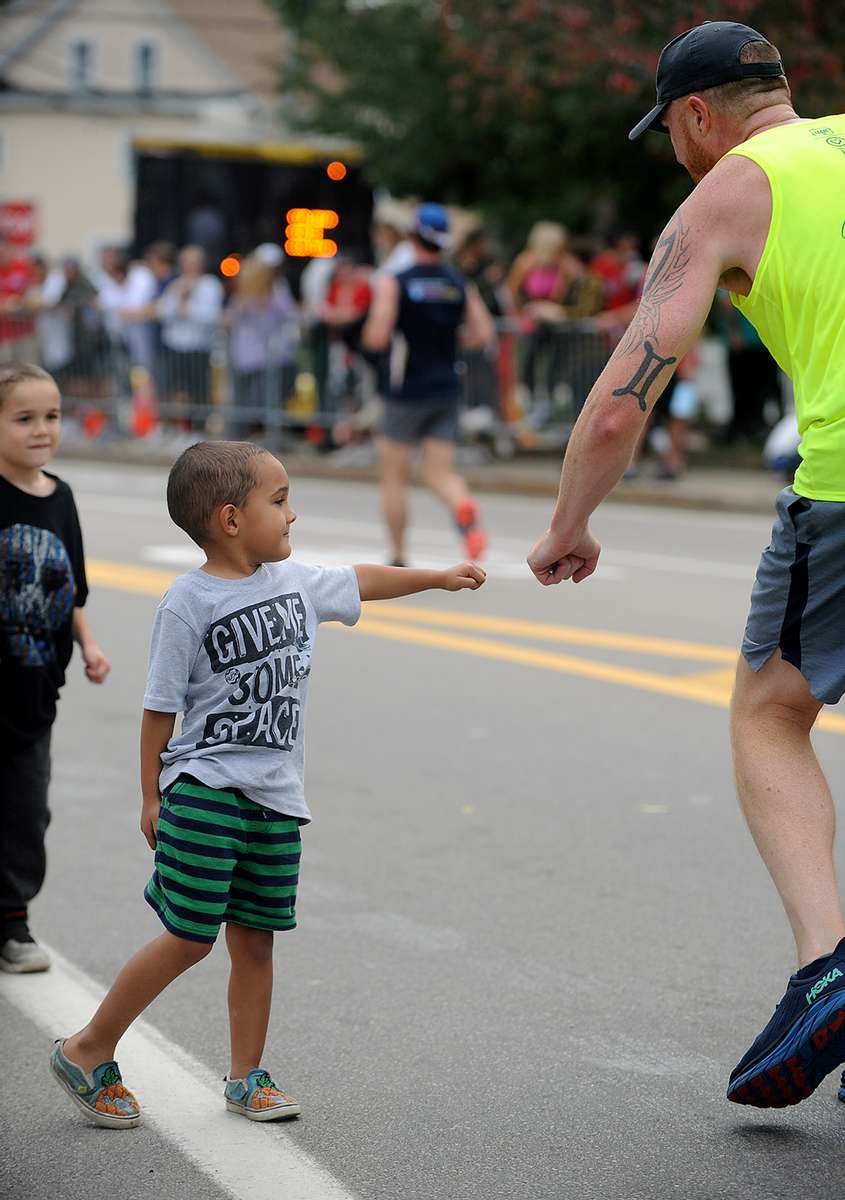 Cruz Florian, 5, and his brother,  Beckam, 7, fist bump runners in Framingham during the running of the 125th Boston Marathon, Oct. 11, 2021.