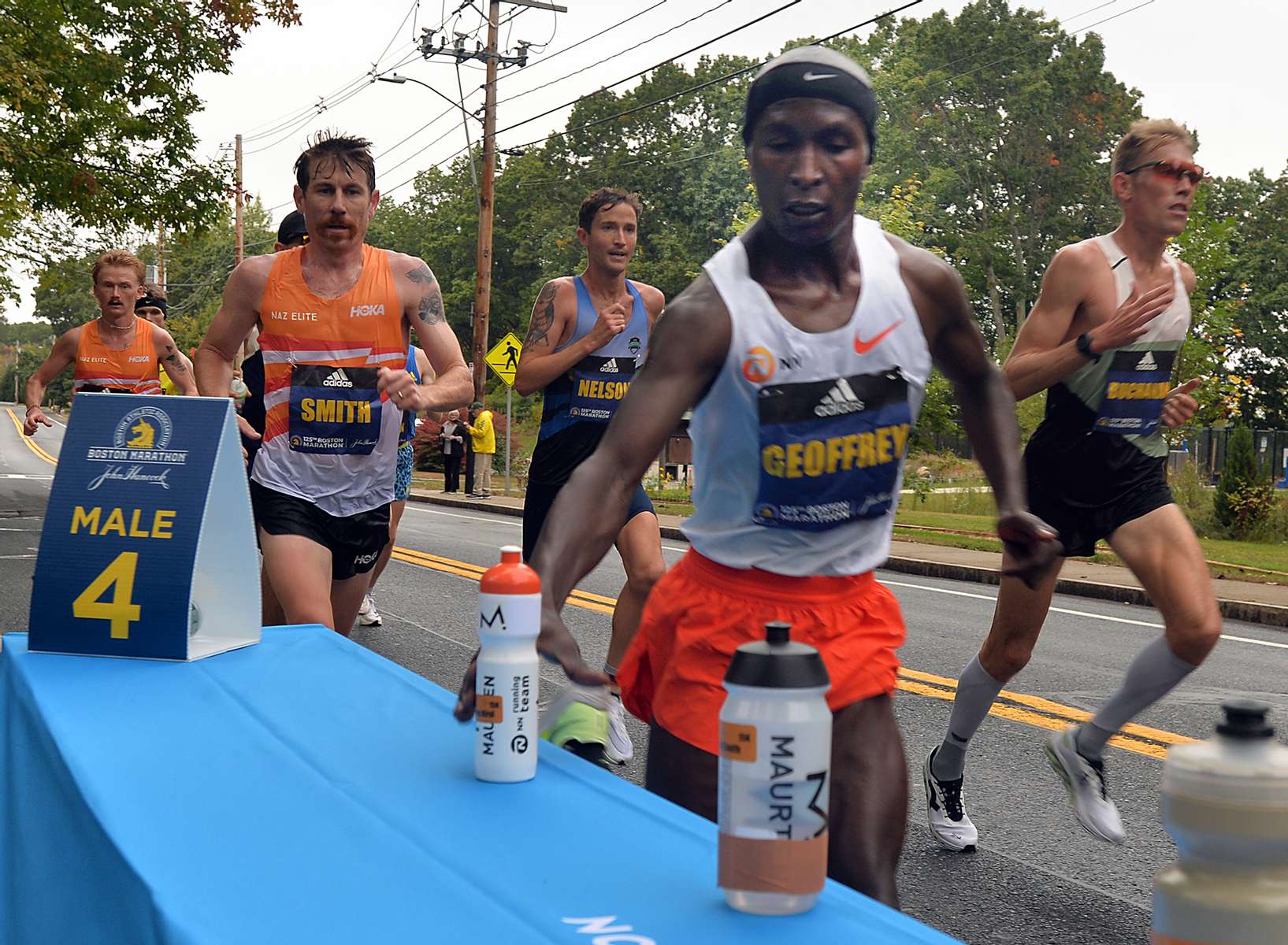 Elite runners pick up their personal water bottles  in Framingham during the running of the 125th Boston Marathon, Oct. 11, 2021.