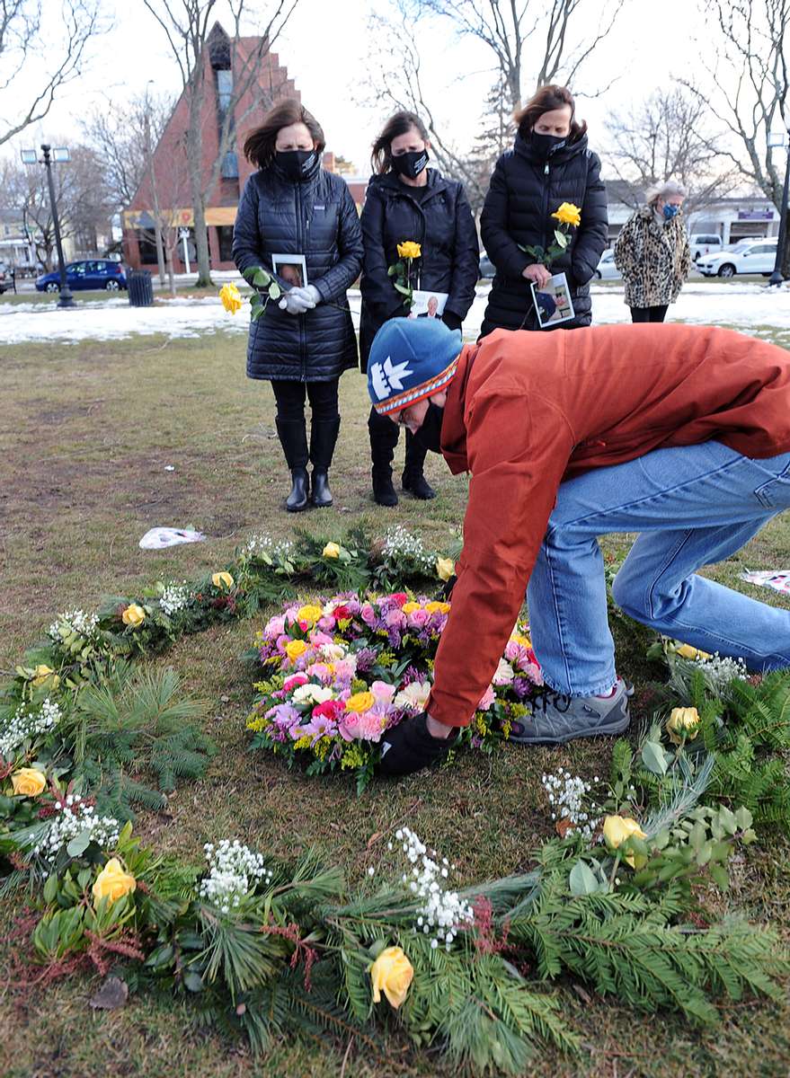 Jill Federman, of Hingham, Lisa Mazerollen, of Easton, and Michelle Pepe, of Sharon, all who recently lost their fathers to COVID-19, watch as David Vaughn, of Natick, places a wreath in  the Floral Heart Project on the Natick Common, March 1, 2021.