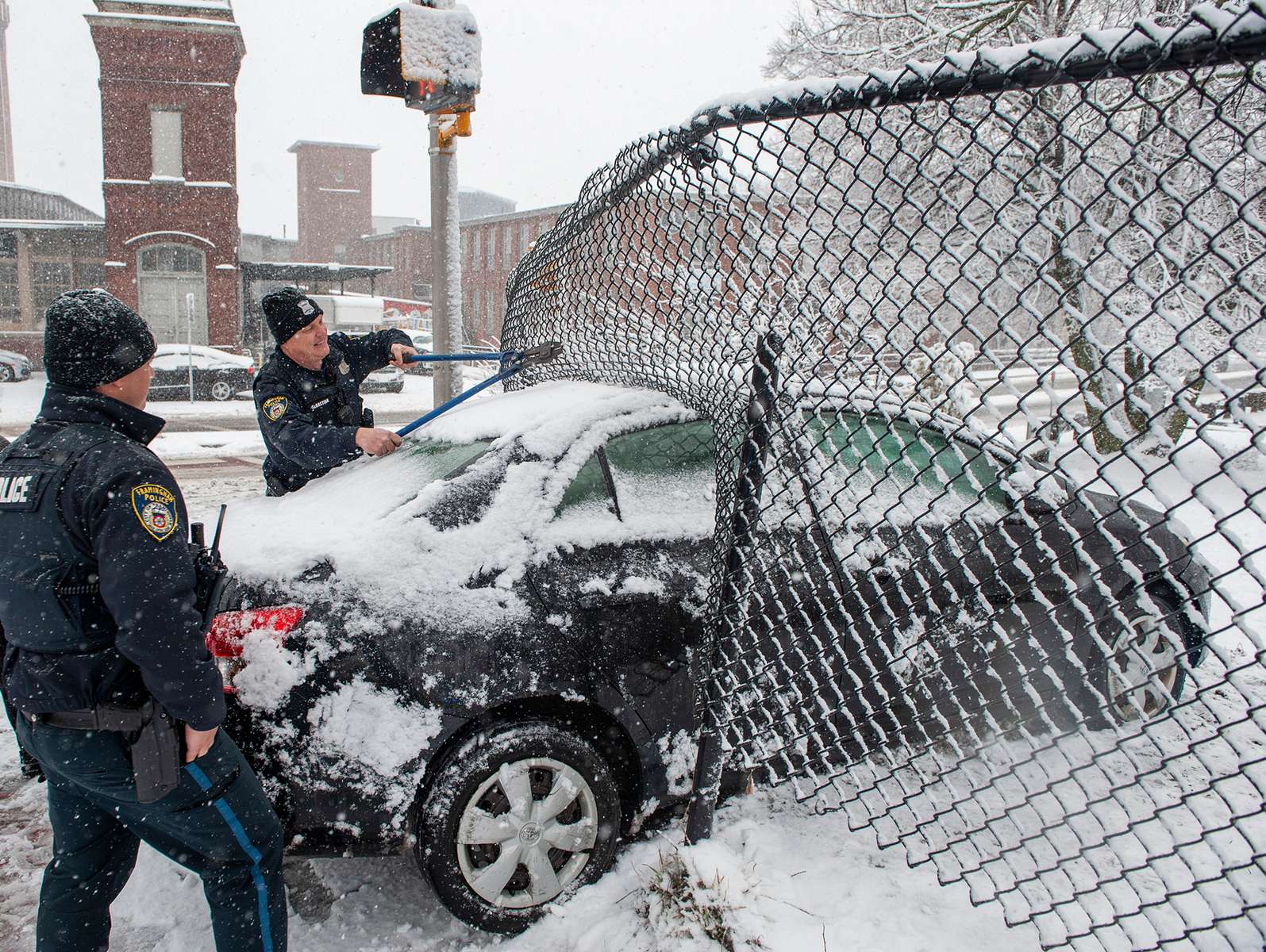 Framingham Police officers help to free a car that slid on the snow tand lodged through a chain link fence at Water Street and Central Street, with the Sudbury River a short distance away, Jan. 23, 2023. 