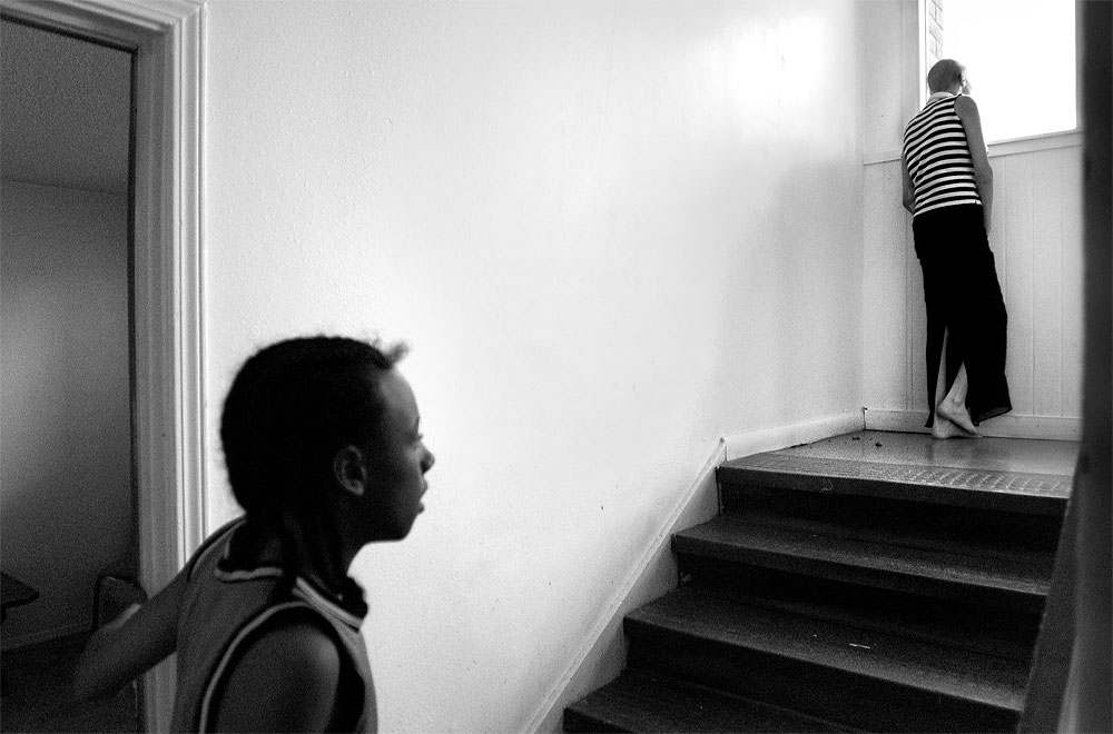 Mooda peeks out a window on the landing of her family's apartment complex to see whether a television from the Make a Wish Foundation has arrived. Mooda can endure only limited exposure to sunlight while the chemotherapy drugs are in her system. Her nephew Abdul Robinson-Rashad keeps watch from the apartment door.