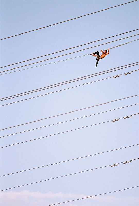 An unidentified man hangs from a power line over the American River in Sacramento, Calif. After cutting his wrists and neck, and threatening to both hang and electrocute himself, he climbed down into police custody. The ordeal on the 115,000 volt power lines caused gas and electricity to be turned off in nearby neighborhoods.