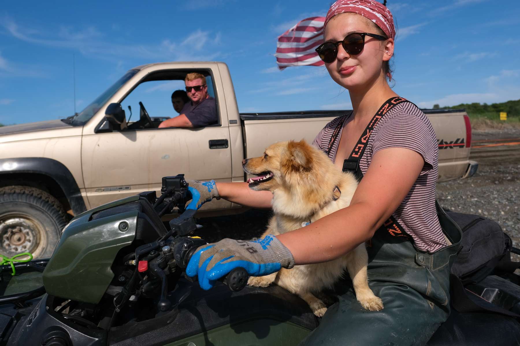 Johnna Bouker, from Dillingham, Alaska, rides a four-wheeler with her dog as her father, John Paul Bouker, looks on, in Ekuk, Alaska on July 4, 2019. 964 setnet permits were fished last year in Bristol Bay. Approximately 60 of those are fished on Ekuk, where fishing families set up seasonal camps.  (Photo by Karen Ducey)