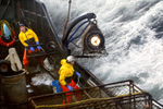 Crewman Lee Fleury prepares to throw the grappling hook at a crab pot buoy off in the distance while Lyndon Yockey (rear) runs the hydrolics to manuever heavy crab pots being stacked onboard. The 2003 Bristol Bay red king crab season lasted 5 days and 2 hours and was plagued with gale force winds of 35 knots or higher almost everyday causing to seas to rise 10 to 15 feet. © copyright Karen Ducey